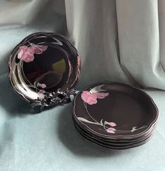 four black plates with pink flowers on them sitting on a blue cloth covered tablecloth