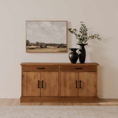 two vases on top of a wooden cabinet in front of a wall with a painting