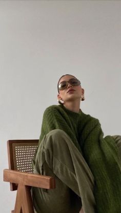 a woman sitting on top of a wooden chair wearing sunglasses and a green blanket over her head