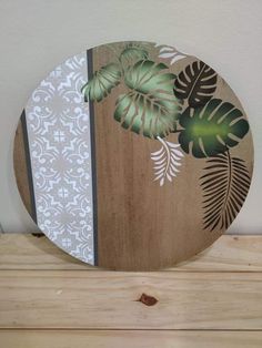 a wooden plate with leaves on it sitting on top of a wood table next to a white wall