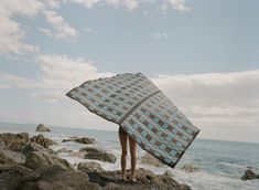 a person standing on rocks with a checkered blanket over their head looking out at the ocean