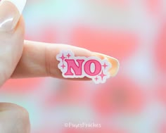 a hand holding a pink sticker with the word no in it's center