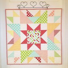 a colorful quilt hanging on the wall with hearts in the backgroung area