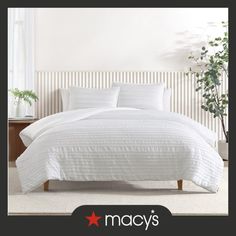 a bed with white comforter and pillows in a room next to a potted plant