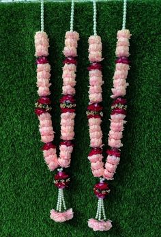 three necklaces made out of pink and white flowers on green grass with beads hanging from them