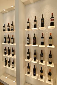 several bottles of wine are on shelves in a room with white shelving and wood flooring