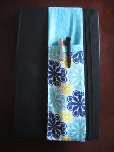 a notebook with a pen in it sitting on top of a wooden table next to a bag