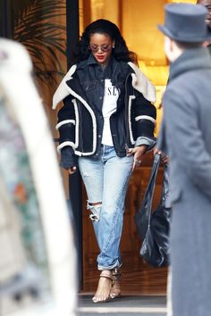 a woman in ripped jeans and a black jacket is walking out of a building with her hand on her hip