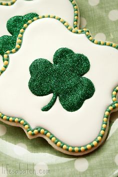 two decorated shamrock cookies sitting on top of a green polka dot tablecloth covered plate