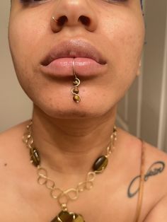 a close up of a person wearing a necklace and nose ring with gold rings on it