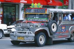 an old jeep driving down the street in front of a building with advertisements on it