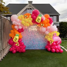 an arch made out of balloons with pineapples and flamingos on it in front of a house