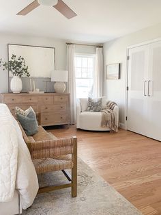 a bedroom with white walls and wood floors, a bed, chair, dresser and mirror