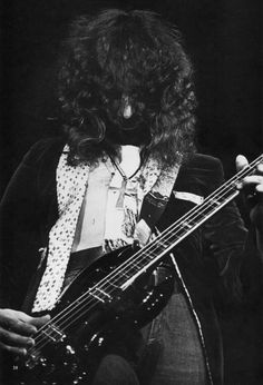 an old photo of a man with long hair playing a bass in front of him