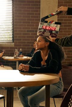 a woman is sitting at a table with a box on her head and another person standing behind her