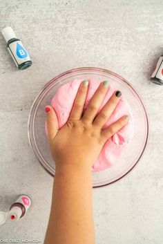 a person's hand on top of a pink substance in a bowl with other items around it