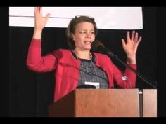 a woman giving a speech at a podium with her hands in the air and one hand up