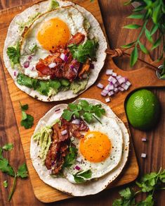 two breakfast tacos with eggs, bacon and avocado on a cutting board