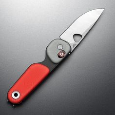 a red and black knife sitting on top of a gray table next to a pair of scissors