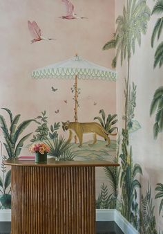 the wallpaper in this room is painted with pink and green palm trees, an umbrella and a cat