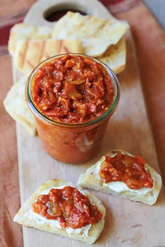 a jar of sauce sitting on top of a wooden cutting board next to crackers