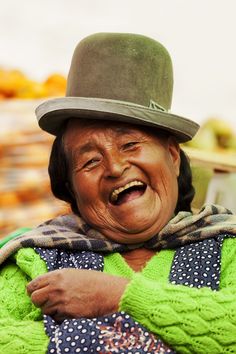 an old woman wearing a green sweater and hat with her hands on her chest smiling