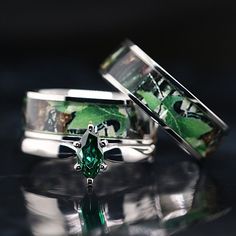 two wedding rings with an emerald colored stone in the middle, on a reflective surface