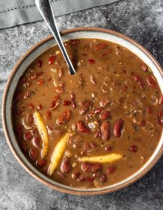 a bowl filled with beans and other food on top of a gray countertop next to a spoon