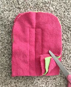 a pair of scissors sitting on top of a pink piece of cloth next to a hole in the fabric