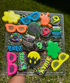 there are many decorated cookies in the tray on the grass, and one is holding it