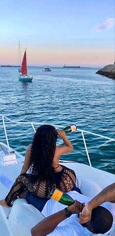 a man and woman are sitting on a boat in the water with sailboats in the background