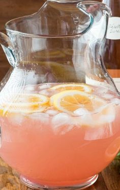 a pitcher filled with pink liquid and lemons on top of a wooden table next to bottles