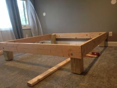 a wooden bed frame sitting on top of a carpeted floor next to a window