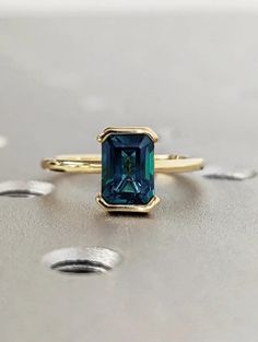 a gold ring with an emerald colored stone in the center on top of a silver surface