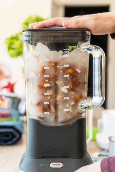 a blender filled with lots of food on top of a wooden table next to a person's hand