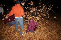 two children playing in leaves with an adult