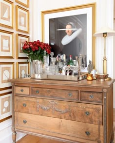 an old dresser with many bottles and glasses on it in front of a framed photograph