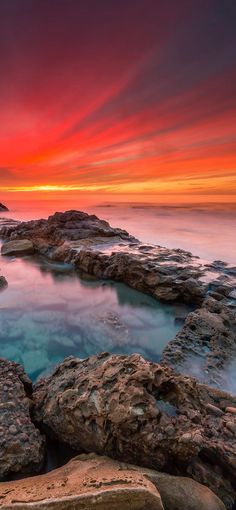 the sun is setting over an ocean with rocks and water in it's foreground