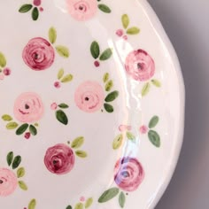 a white plate with pink and green flowers painted on the side, sitting on a table