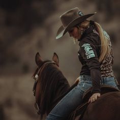 a woman riding on the back of a brown horse wearing a cowboy hat and jeans