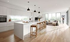 an open kitchen and living room with white cabinets, wood flooring and large windows