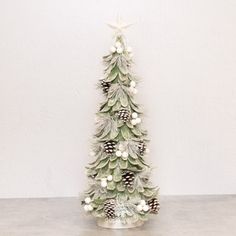 a small christmas tree with pine cones and white balls on it's branches, in front of a white wall