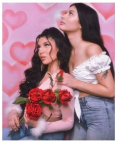 two beautiful women standing next to each other in front of a wall with hearts on it