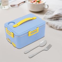 a blue and yellow lunch box sitting on top of a table next to utensils