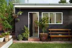 a black house with potted plants and a wooden bench in the front garden area