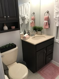 a white toilet sitting next to a sink in a bathroom under a mirror with pink towels on it