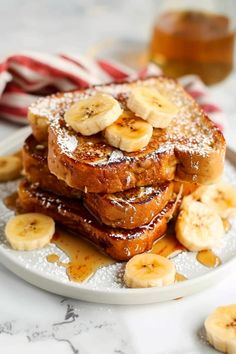 french toast topped with bananas and powdered sugar on a white plate next to sliced bananas