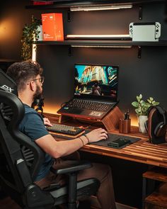 a man sitting in front of a laptop computer on top of a wooden desk with headphones