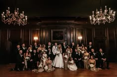 a large group of people in formal wear posing for a wedding photo with chandeliers