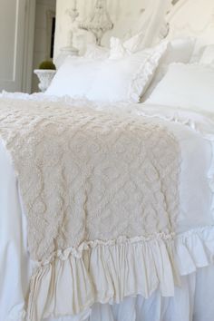 a white bed with ruffled bedspread and pillows